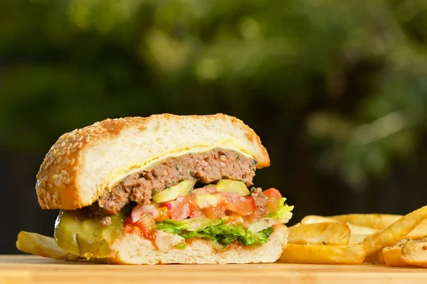 Burger tăiat cu brânză topită și carne de vită suculentă groasă, salată verde, roșii, ceapă, coc de susan în picioare pe masă de lemn — Fotografie, imagine de stoc