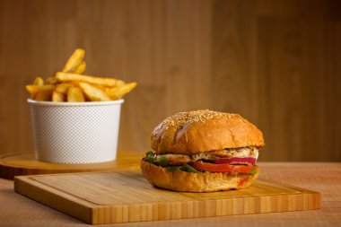Eritilmiş peynir ve kalın etli kara tavuk patty, marul, domates, soğan, ahşap masa üzerinde duran susam çörek ile lezzetli burger
