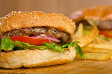 Eritilmiş peynir ve kalın etli zemin sığır patty, marul, domates, soğan, ahşap masa üzerinde duran susam çörek ile lezzetli burger