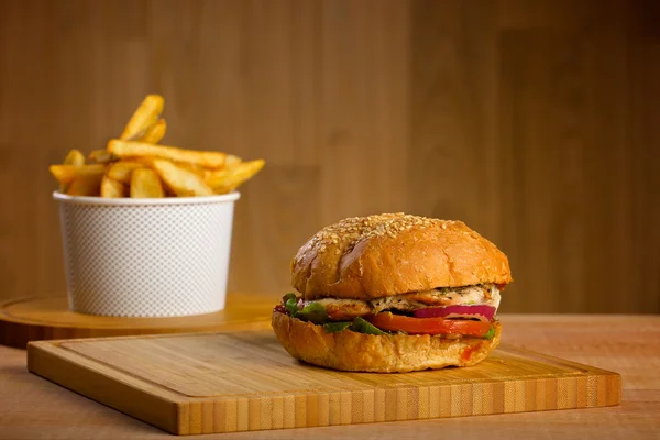 Hamburger savoureux au fromage fondu et épaisse galette de poulet haché succulent, laitue, tomate, oignon, pain au sésame debout sur une table en bois — Photo