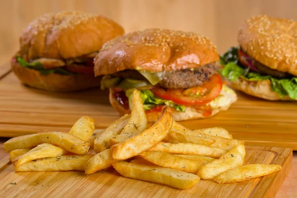 Sabrosa hamburguesa con queso derretido y carne molida suculenta gruesa empanada, lechuga, tomate, cebolla, pan de sésamo de pie sobre una mesa de madera —  Fotos de Stock