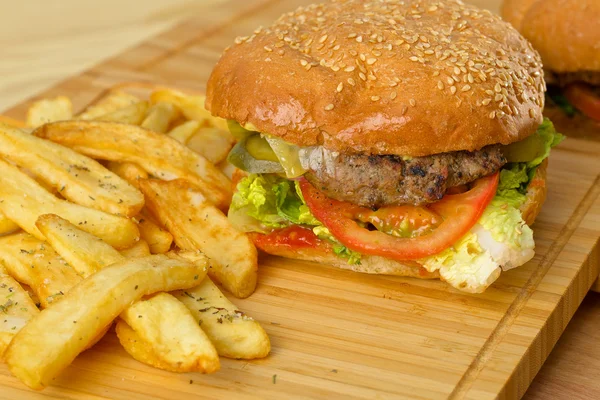 Burger lezat dengan keju yang meleleh dan patty daging sapi, selada, tomat, bawang, roti wijen tebal berdiri di atas meja kayu — Stok Foto