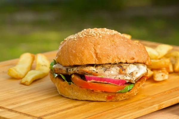 Sabrosa hamburguesa con queso derretido y carne molida suculenta gruesa empanada, lechuga, tomate, cebolla, pan de sésamo de pie sobre una mesa de madera — Foto de Stock
