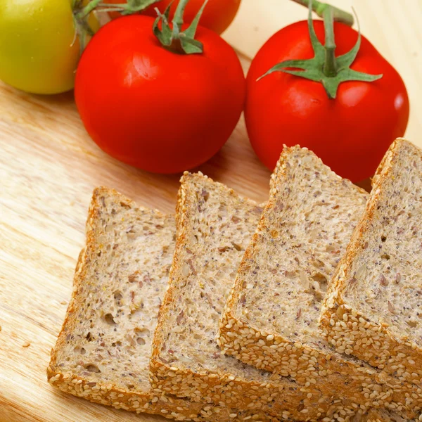Rye bread slices and tomatoes on wooden table — Stock Photo, Image