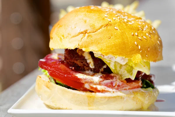 Hambúrguer saboroso com queijo derretido e carne moída suculenta grossa, alface, tomate, cebola, pão de gergelim em pé na mesa de madeira — Fotografia de Stock