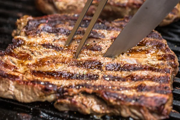 Beef steaks on grill with BBQ fork and knife — Stock Photo, Image