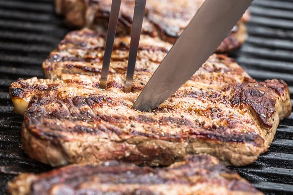 Bifes de carne na grelha com garfo e faca para churrasco — Fotografia de Stock