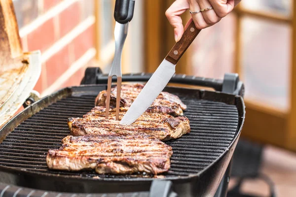 Beef steaks on grill with BBQ fork and knife — Stock Photo, Image