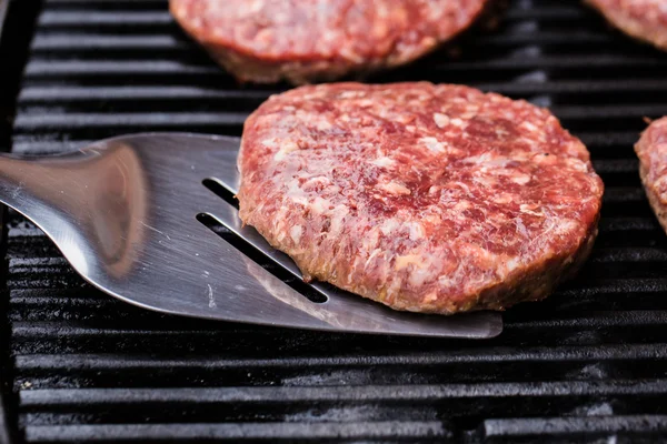 Grilled ground beef pattie burger on spatula against BBQ — Stock Photo, Image