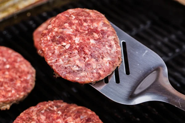 Grilled ground beef pattie burger on spatula against BBQ