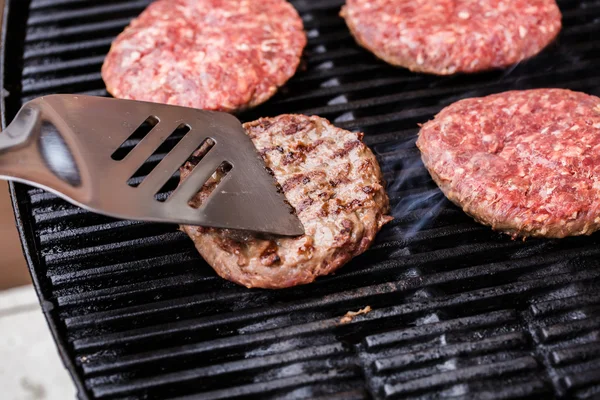 Hambúrguer de carne moída grelhada na espátula contra churrasco — Fotografia de Stock
