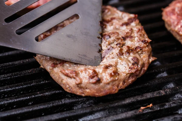 Grilled ground beef pattie burger on spatula against BBQ — Stock Photo, Image