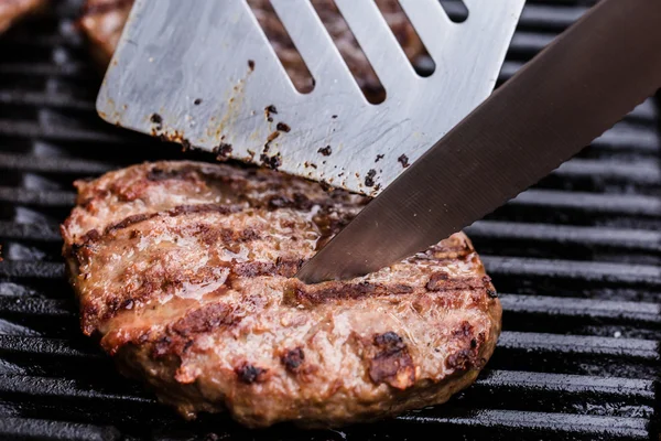 Grilled ground beef pattie burger with spatula and knife on BBQ — Stock Photo, Image