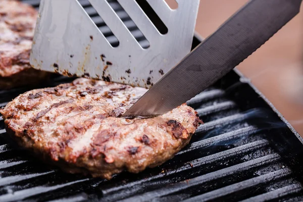 Grilled ground beef pattie burger with spatula and knife on BBQ — Stock Photo, Image