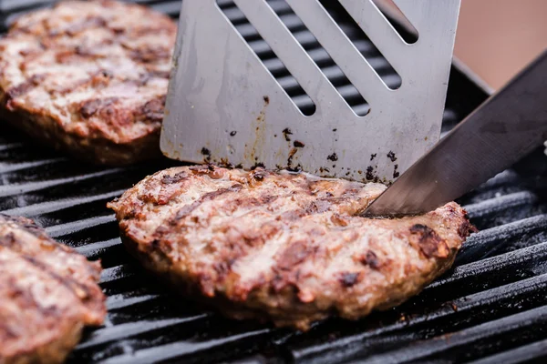 Burger de carne de vită la grătar cu spatulă și cuțit pe grătar — Fotografie, imagine de stoc