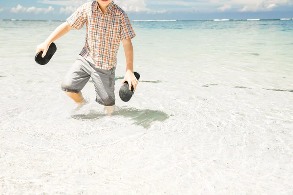 Szczęśliwy młody chłopiec przebywa w wody oceanu na pięknej plaży na sobie kapelusz i okulary. — Zdjęcie stockowe