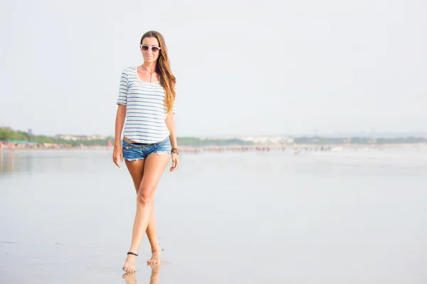 Beautiful young woman walking along the beach at sunset enjoing summer vacation — стоковое фото