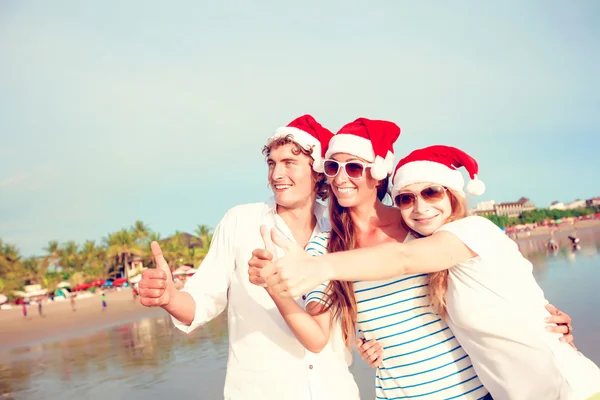 Groupe de jeunes gens heureux en chapeaux de Noël sur la plage — Photo