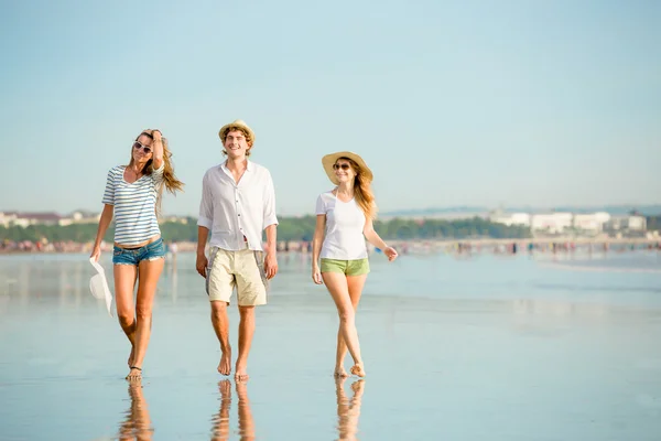 Group of happy young people walking along the beach on beautiful summer sunset — Stock Photo, Image