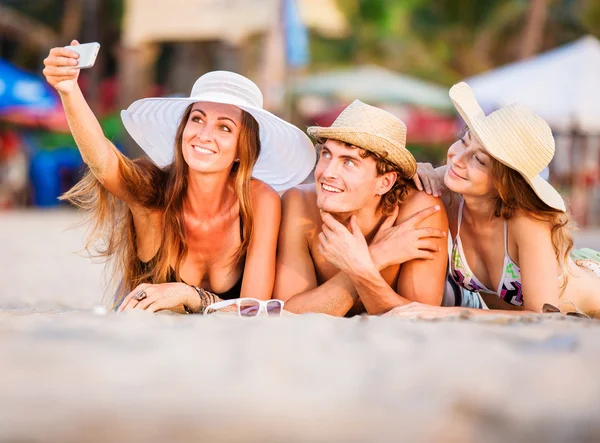 Gruppo di giovani felici sdraiati sulla sabbia bianca della spiaggia e scattare foto di selfie — Foto Stock