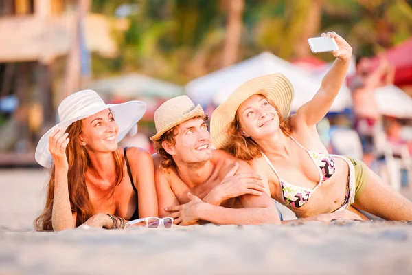 Group of happy young people lying on wite beach sand and taking selfie photo — Stock Photo, Image