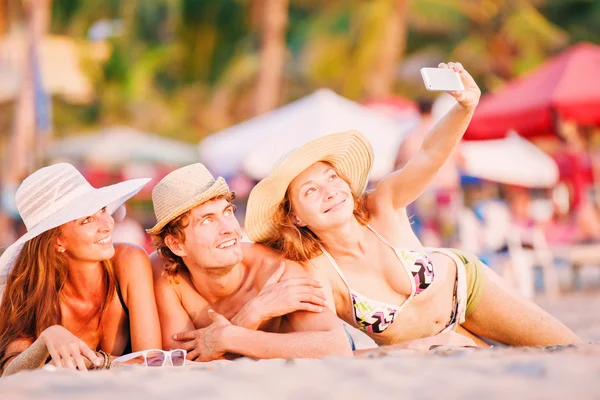 Group of happy young people lying on wite beach sand and taking selfie photo