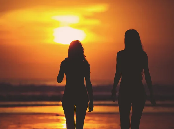 Silhouettes of two girls against red sunset on the beach — Stock Photo, Image