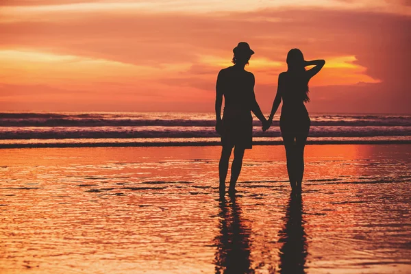 Siluetas de pareja joven en el amor staing en la playa con hermosa puesta de sol roja como fondo —  Fotos de Stock