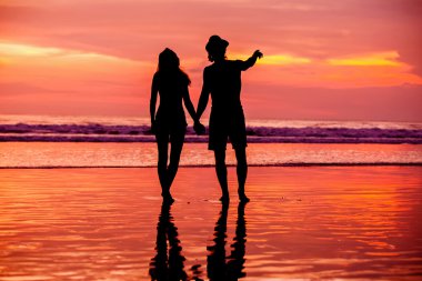 Silhouettes of young couple in love staing on the beach with beautiful red sunset as background clipart