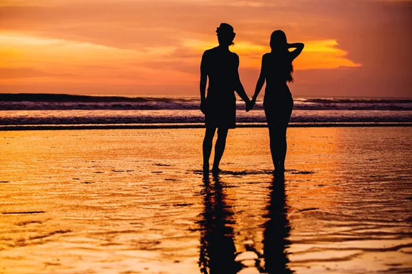 Siluetas de pareja joven en el amor staing en la playa con hermosa puesta de sol roja como fondo — Foto de Stock