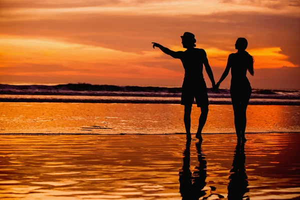 Siluetas de pareja joven en el amor staing en la playa con hermosa puesta de sol roja como fondo — Foto de Stock