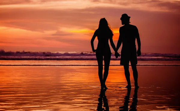 Silhouettes of young couple in love staing on the beach with beautiful red sunset as background — Stock Photo, Image