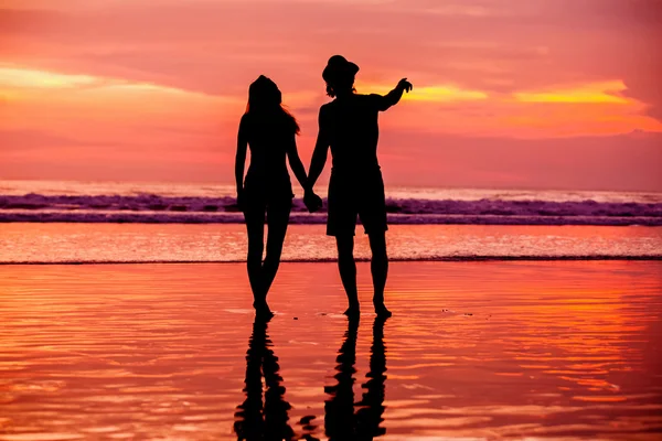 Silhouettes of young couple in love staing on the beach with beautiful red sunset as background — Stock Photo, Image