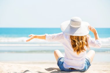 Güneşli bir günde sahilde oturan güzel genç bir kadın yaz tatilini kutluyor.