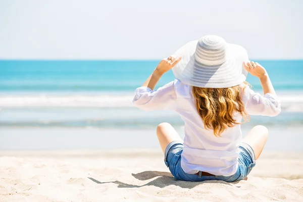 Güneşli bir günde sahilde oturan güzel genç bir kadın yaz tatilini kutluyor.