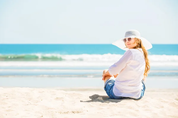 Красивая молодая женщина сидит на пляже в солнечный день наслаждаясь летними каникулами — стоковое фото