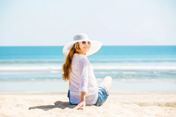 Güneşli bir günde sahilde oturan güzel genç bir kadın yaz tatilini kutluyor. — Stok fotoğraf