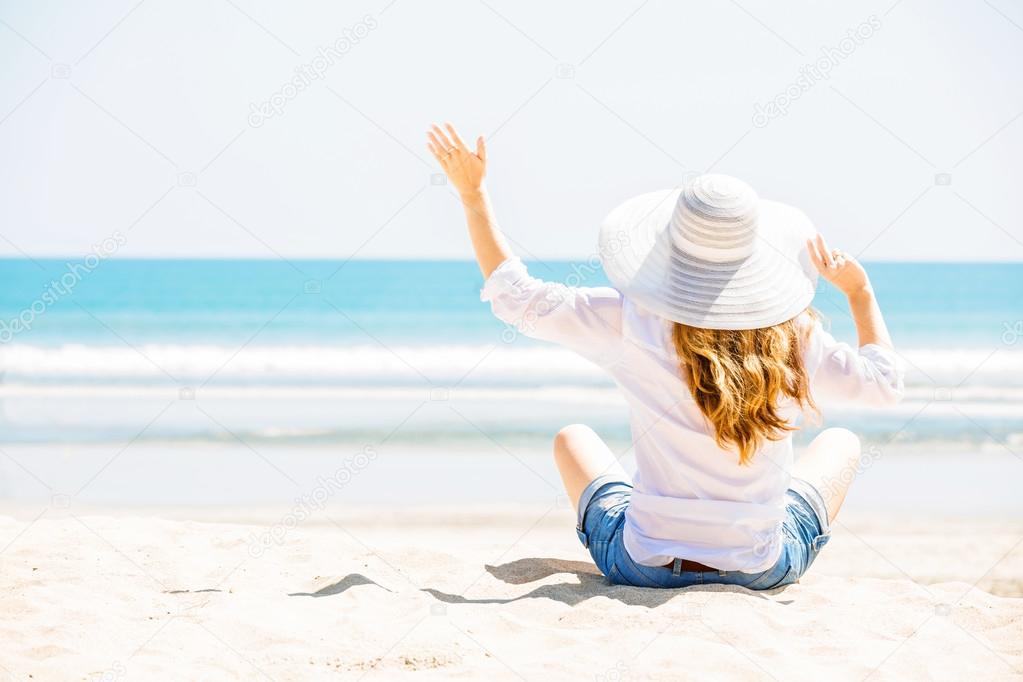 Beautifil young woman sitting on the beach at sunny day enjoing summer vacation