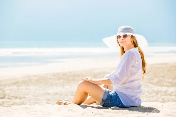 Beautifil Mujer joven sentada en la playa en un día soleado disfrutando de las vacaciones de verano —  Fotos de Stock