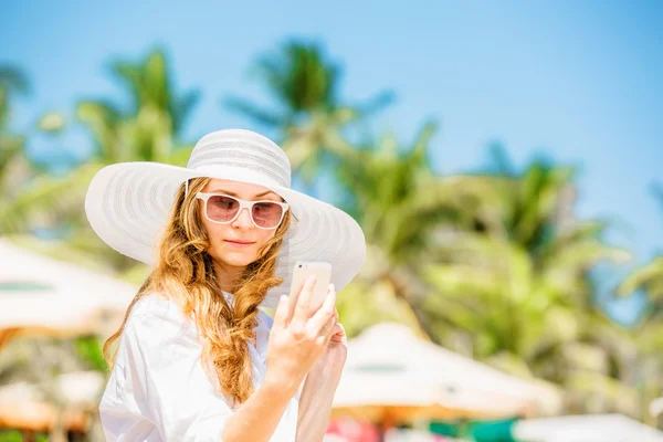 Beautifil young woman sitting on the beach at sunny day with phone in her hand — Stock Photo, Image