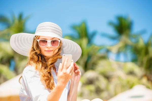 Beautifil young woman sitting on the beach at sunny day with phone in her hand — Stock Photo, Image