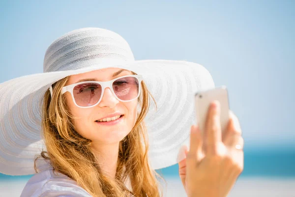 Beautifil young woman sitting on the beach at sunny day with phone in her hand — Stock Photo, Image