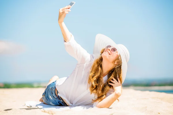 Beautifil young woman lying on the beach at sunny day and taking selfie with phone — Stock Photo, Image