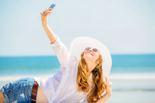 Beautifil young woman lying on the beach at sunny day and taking selfie with phone — Stock Photo, Image