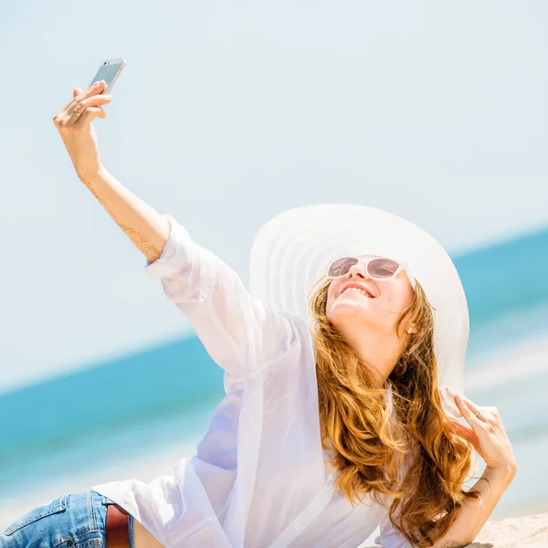 Beautifil young woman lying on the beach at sunny day and taking selfie with phone — Stock Photo, Image