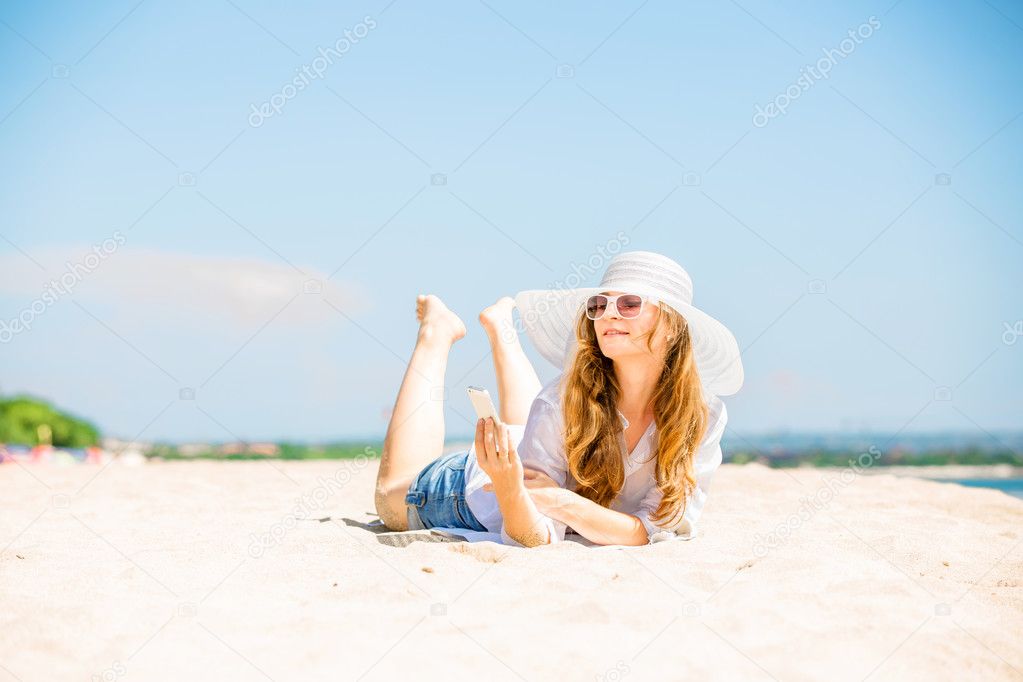 Beautifil young woman lying on the beach at sunny day with phone in her hand