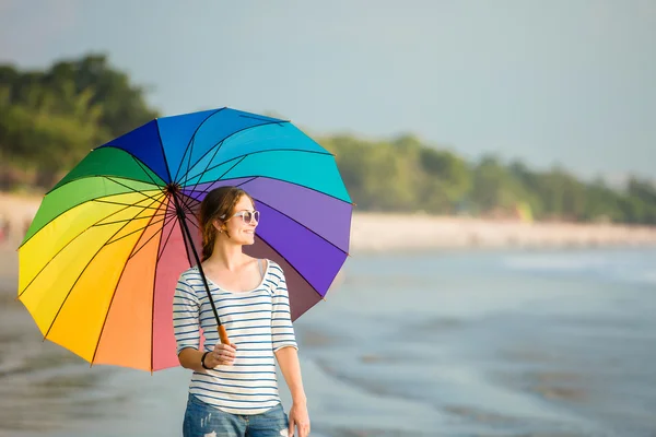 Young caucasian woman wearing sunglasses with colourful rainbow umbrella looking at ocean on the beach before sunset. Travel, holidays, vacation, healthy lifestyle concept — Stock Photo, Image