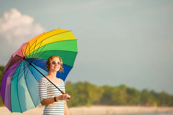 Young caucasian woman wearing sunglasses with colourful rainbow umbrella looking at ocean on the beach before sunset. Travel, holidays, vacation, healthy lifestyle concept — Stock Photo, Image