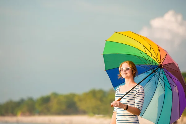 Young caucasian woman wearing sunglasses with colourful rainbow umbrella looking at ocean on the beach before sunset. Travel, holidays, vacation, healthy lifestyle concept — Stock Photo, Image