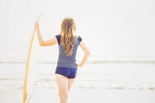 Beautiful young surfer girl stays on the beach at sunset with yellow surfboard. Healthy lifestyle, leisure, travel, holiday and sport concept, copyspace — Stock Photo, Image